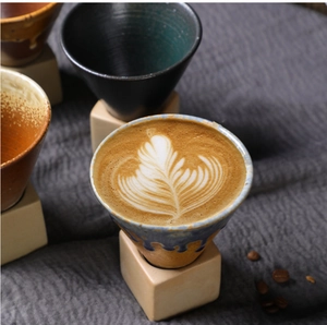 Macro detail of stoneware coffee mug with blue reactive glaze and latte art on wooden base