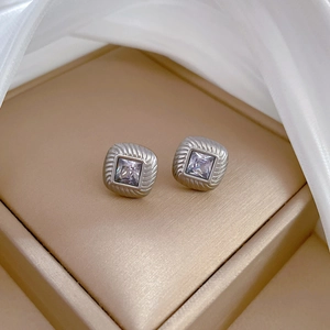 Macro detail of silver titanium steel earrings with square purple zircon on silk