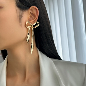 Dettaglio orecchini a fiocco dorati oversize con frange metalliche su modella