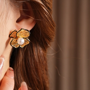 Detail of gold floral earring with woven texture, black enamel edges, and central pearl