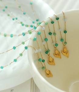 Detail of vintage gold tulip necklaces with green crystal beads hanging on a cream bowl