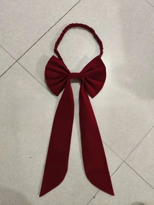 Close-up of a large dark red satin bow with long flowing ribbons and elastic headband