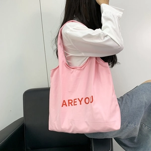 Pink canvas tote bag with red letter print shown with model for a casual look