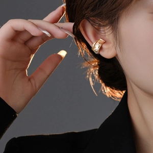 Fashionable gold textured ear bone clip with zircon accents on model with dark background