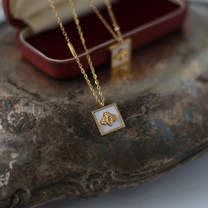 Macro detail of square gold bee pendant with white mother of pearl inlay on 18K plated chain