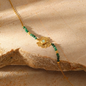 Macro shot of gold flower pendant with green gemstone on natural rock and sand base