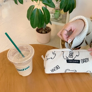 Close-up of cream corduroy pencil case with bear print and metal zipper on wooden table