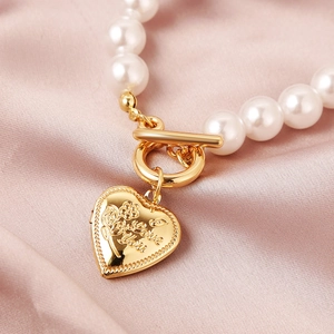 Macro shot of gold heart pendant with rose relief and I love you engraving on pearl bracelet