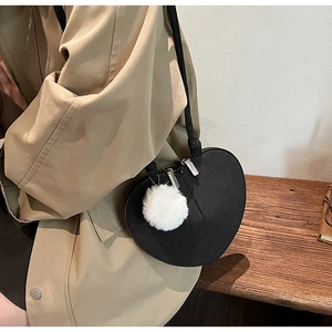 Detail der herzförmigen Umhängetasche mit mattem Finish und weißem Bommel-Anhänger