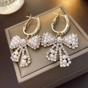 Dettaglio di orecchini a fiocco dorati con perle bianche e strass brillanti e rifiniti