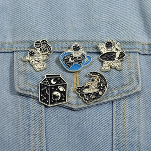 Detailed view of five space enamel pins featuring cartoon astronauts on blue denim fabric