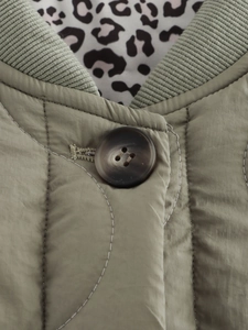 Close-up of olive green quilted jacket with ribbed collar, tortoise button and leopard lining
