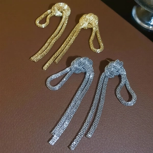 Detail of gold and silver knot tassel earrings on a textured leather surface