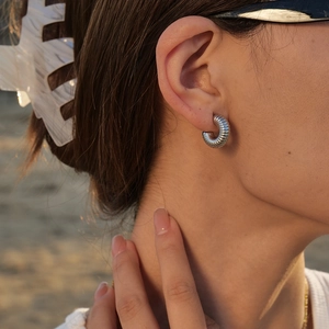 Detailed close-up of silver hollow hoop earrings with textured spiral design on ear