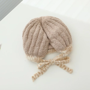 Detail of baby knit hat showing soft beige yarn texture and bow strap tie closure