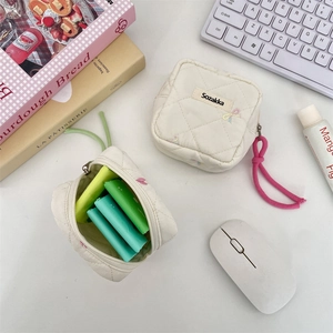 Detail showing a cream quilted mini storage pouch for sanitary pads on a desk