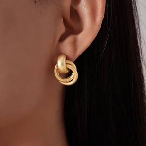 Gros plan de boucles d'oreilles géométriques entrelacées en or mat sur un mannequin
