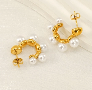 Detail view of gold C-shaped stainless steel earrings with elegant white pearls