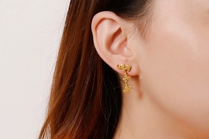 Close-up of golden elephant and heartbeat line stud earring worn on ear detail
