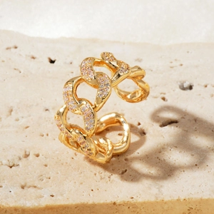 Detail of gold chain link ring with pavé cubic zirconia on textured stone background