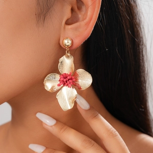 Detailed view of golden floral earrings with red pistil detail on a fashion model