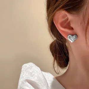 Minimalist silver heart stud earrings with a polished finish worn by a model
