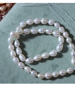 Close-up of 5-6mm white rice-shaped freshwater pearls on a green velvet texture