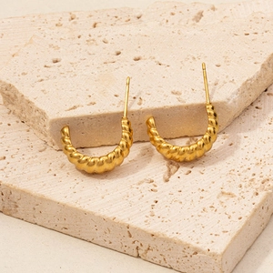 Macro view of gold 304 stainless steel croissant hoop earrings on stone background