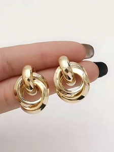 Macro detail of triple interconnected golden alloy hoop earrings held to show scale