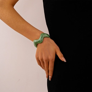 Detail of a wavy green acrylic marble bangle worn by a model against black and white background