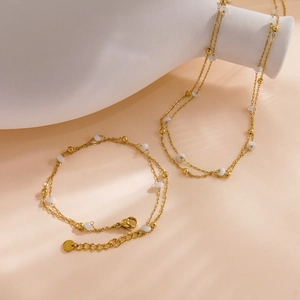 Elegant gold double-layer necklace and bracelet set with white beads on a ceramic plate