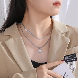 Detail of silver double-layered necklace featuring snake chain and queen coin pendant