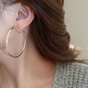Close-up of a large gold round hoop earring worn by a model in warm lighting