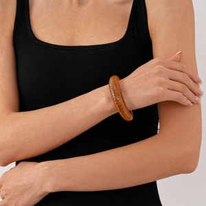 Detail of amber acrylic bangle with retro textures on wrist of model wearing black vest