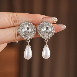Close-up of silver drop earrings with square crystal studs and white teardrop pearls