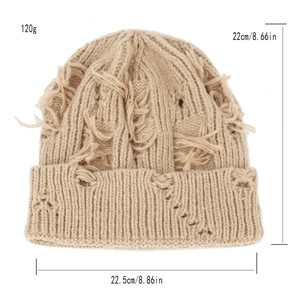 Close-up of distressed beige knit beanie showing frayed hole details and soft yarn texture