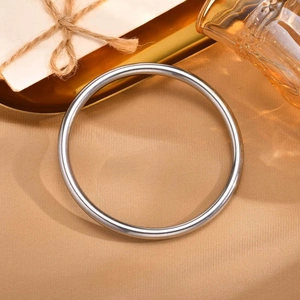 Close-up of a minimalist polished silver round metal bangle on elegant golden silk fabric