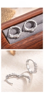 Close-up of silver hoop earrings with wavy edges and three sparkling zircon stones