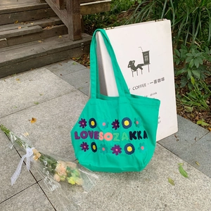 Detail view of a green canvas tote bag with floral embroidery and text in an outdoor setting