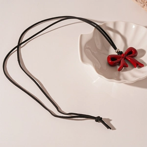 Macro detail of red resin bow pendant with black suede cord on a white shell plate