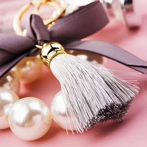 Detail of white pearls, deep purple velvet bow, and grey tassel on a metal keychain