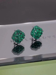 Macro shot of green geometric diamond earrings reflected on a mirror with text