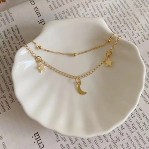 Double-layered gold moon and star pendant anklet displayed on a white shell plate