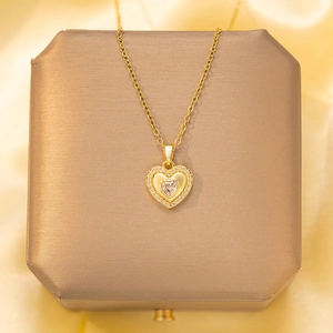 Elegant gold heart pendant necklace with shimmering zircon stones on warm silk background