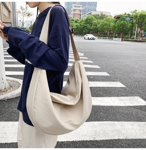 Beige oversized nylon crescent crossbody bag styled with a wide adjustable shoulder strap