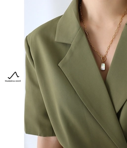 Gros plan d'un collier en acier doré avec pendentif en nacre sur un mannequin en costume