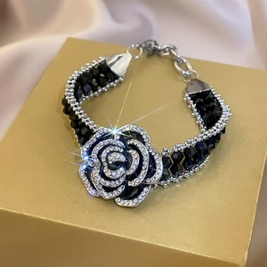 Macro shot of silver camellia pendant with rhinestones on black crystal beaded bracelet