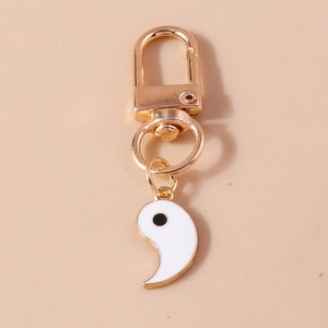 Golden keychain with Tai Chi Yin Yang white enamel pendant on a minimal beige background