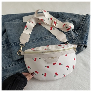 Close-up of white crossbody bag with cherry prints on blue denim jacket and white sheets