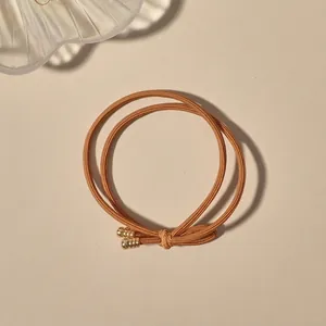 Macro detail of high-elastic braided hair tie in brown gold with dual metal screw-end beads